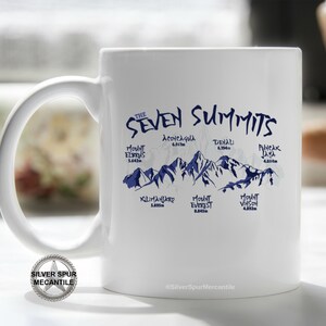 May include: White ceramic mug with a blue graphic of the Seven Summits mountains and their names and elevations in meters. The text "THE SEVEN SUMMITS" is at the top of the mug. The text "@SilverSpurMercantile" is at the bottom of the mug.