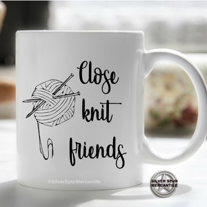 Może przedstawiać: Biały kubek ceramiczny z czarno-białym rysunkiem wł&oacute;czki i drut&oacute;w do rob&oacute;tek na drutach. Na kubku nadrukowany jest tekst "Close knit friends".