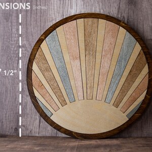 May include: A round wooden decorative piece with a sunburst design. The piece is 7 1/2 inches in diameter. The sunburst features alternating wooden panels in shades of brown, pink, and blue, set within a dark brown frame.