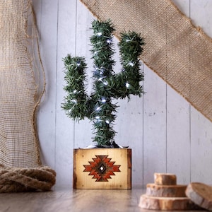 May include: A decorative cactus-shaped artificial plant with white string lights, set in a wooden box. The box features a Southwestern-style geometric design in red and brown. The cactus is approximately 24 inches tall.