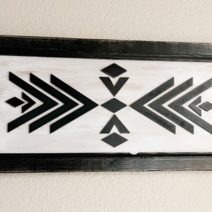 Może przedstawiać: Czarno-biały wz&oacute;r geometryczny w czarnej drewnianej ramie. Wz&oacute;r zawiera szereg strzałek skierowanych w przeciwne strony.