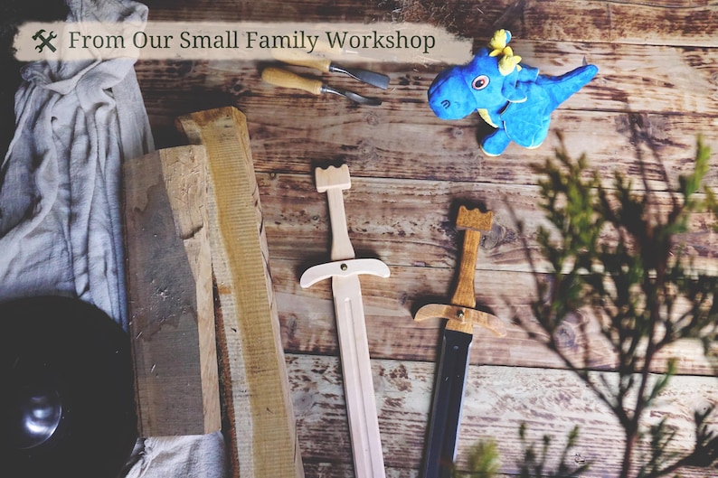 May include: Wooden toy swords with a light wood finish and a black blade, alongside a blue plush dragon toy. The image includes the text "From Our Small Family Workshop" and is set on a rustic wooden surface.