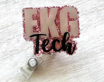 Könnte beinhalten: Ein Ausweis-Rollhalter mit den Worten "EKG Tech" in weißer und schwarzer Schrift. Das Abzeichen hat einen rosafarbenen Glitzerrahmen und eine transparente Kunststoffrolle mit einem Metallclip. Das Abzeichen ist zum Anbringen an Kleidung bestimmt.