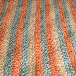 May include: A crocheted blanket with stripes of peach, light blue, and white. The blanket is made with a star stitch pattern.