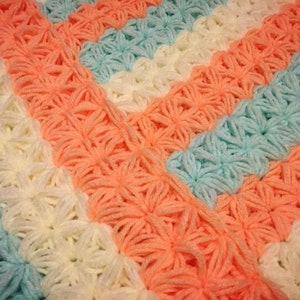 May include: A crocheted blanket with stripes of peach, white, and light blue. The blanket is made with a textured stitch that creates a flower-like pattern.