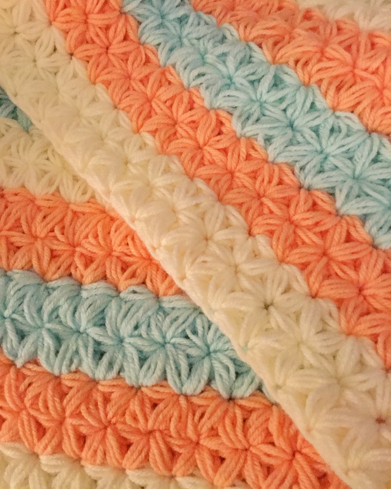 May include: A crocheted blanket with stripes of peach, light blue, and cream.