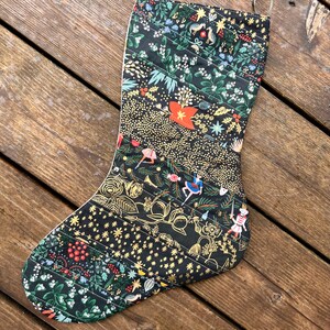 May include: A black Christmas stocking with a gold and green patterned design featuring a variety of holiday motifs, including stars, birds, and a nutcracker.