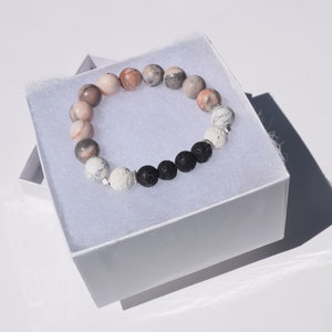 Op de afbeelding: Een kralenarmband met roze, witte en zwarte kralen in een witte doos. De armband is gemaakt van natuurlijke stenen en lavakralen.