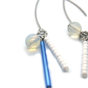 May include: A pair of dangle earrings with blue and white beads. The earrings feature a single, clear, round bead at the top of each earring.