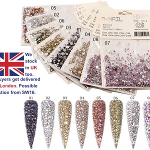 May include: Assortment of eight small bags of assorted clear, iridescent, and coloured rhinestones. Each bag is labelled with a number from 01 to 08. The bags are arranged in a row, with the numbers increasing from left to right. The text "A-NAIL" is visible on the top right bag. The text "M-Foiled Hotfix" is visible on the bag. The text "10 gr/sa = 1,410pcs" is visible on the bag. The text "Os 0152 0153 0154 0155 0156" is visible on the bag. The text "Dk-Tescertified" is visible on the bag.
