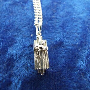 May include: A silver charm necklace with a gift box pendant. The box is detailed with a bow and lines. The chain is a silver curb chain.