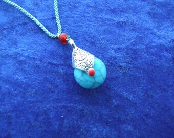 Puede incluir: Un collar con un colgante turquesa y plateado con una cuenta roja. El colgante tiene forma de lágrima con un diseño de filigrana plateada.