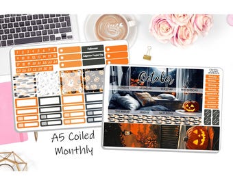 May include: Two sheets of planner stickers with a Halloween theme. One sheet features orange and black boxes, calendar dates, and patterned designs. The other sheet has a cozy October scene with a pumpkin and the days of the week. Text reads "A5 Coiled Monthly".