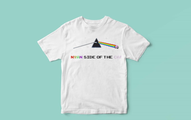 Pu&ograve; includere: Maglietta bianca con un prisma arcobaleno e un gatto rosa con un fumetto che dice "NYAN". Il testo sotto il prisma dice "NYAN SIDE OF THE CAT".