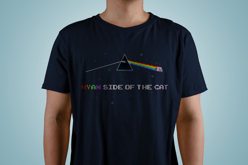 Pu&ograve; includere: Una t-shirt blu navy con un'immagine pixelata di un arcobaleno e un gatto che vola nello spazio. Il testo "NYAN SIDE OF THE CAT" &egrave; stampato sotto l'immagine.