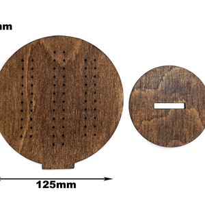 May include: A wooden game board with a circular playing surface and a separate circular base. The playing surface has a pattern of holes and the base has a slot cut out. The board measures 125 mm in diameter.