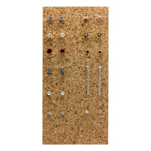 Puede incluir: Un tablero de corcho con una variedad de pendientes expuestos. Los pendientes est&aacute;n hechos de diferentes materiales, incluyendo metal, vidrio y pl&aacute;stico. Vienen en una variedad de colores, incluyendo plata, oro, azul, rojo y blanco.