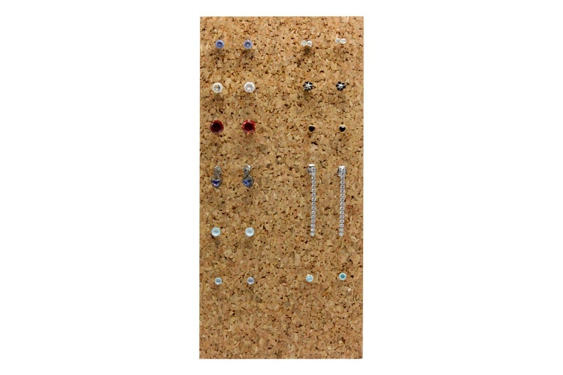 Puede incluir: Un tablero de corcho con una variedad de pendientes expuestos. Los pendientes est&aacute;n hechos de diferentes materiales, incluyendo metal, vidrio y pl&aacute;stico. Vienen en una variedad de colores, incluyendo plata, oro, azul, rojo y blanco.