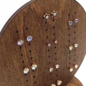 May include: A wooden earring display stand with a variety of earrings featuring different coloured gemstones. The earrings are arranged in rows on the stand.
