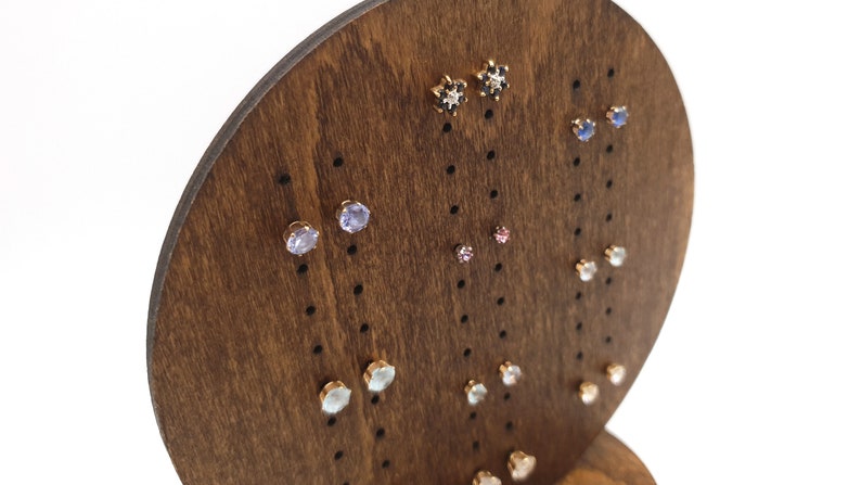 May include: A wooden earring display stand with a variety of earrings featuring different coloured gemstones. The earrings are arranged in rows on the stand.