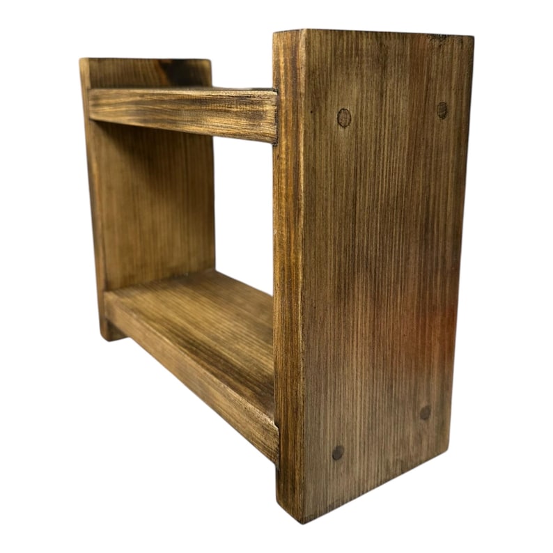May include: A small, rustic wooden shelf with two tiers. The shelf is constructed from stained wood, showcasing visible wood grain and nail heads. The design is simple and functional, suitable for displaying small items or organizing essentials.