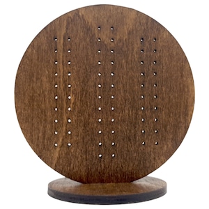 May include: A round wooden earring display stand with a brown stain. The stand has multiple holes for displaying earrings.
