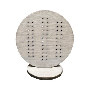 May include: A wooden earring display stand with a circular top and a round base. The top has a pattern of small holes for holding earrings.