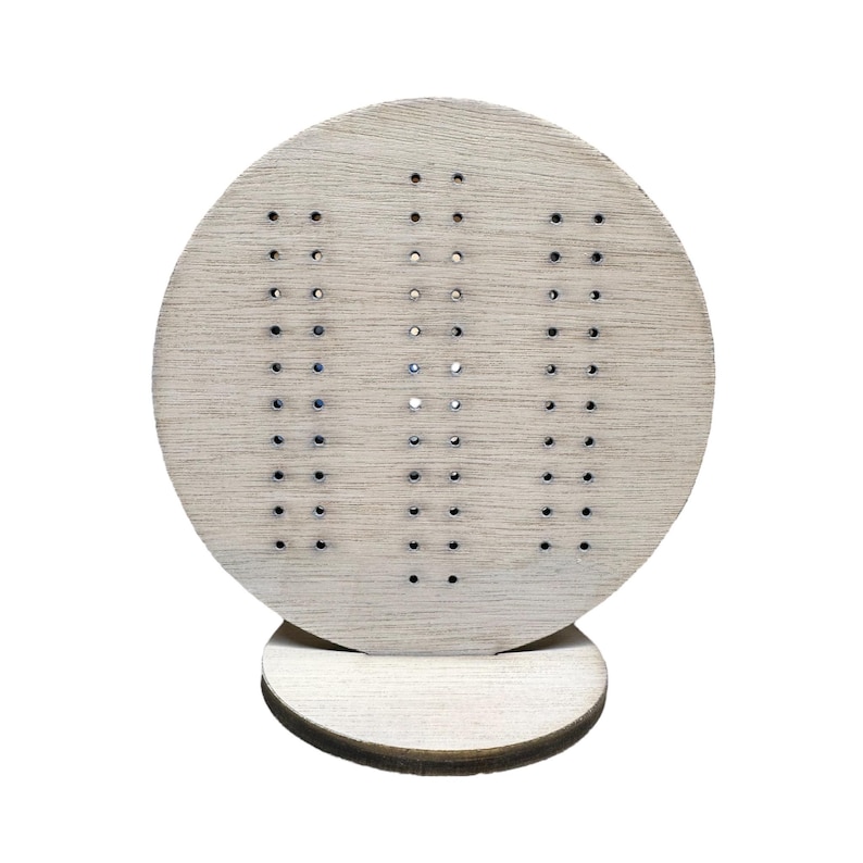 May include: A wooden earring display stand with a circular top and a round base. The top has a pattern of small holes for holding earrings.