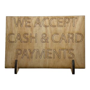 Może przedstawiać: Drewniany znak z tekstem "WE ACCEPT CASH & CARD PAYMENTS" w białych obramowanych literach.