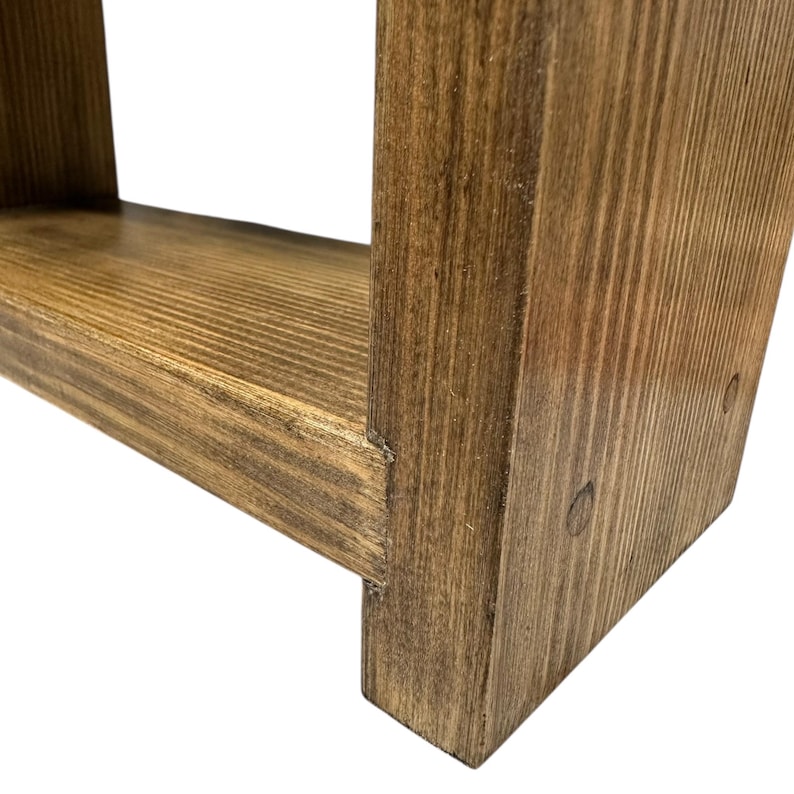 May include: Close-up of a handcrafted wooden shelf with a warm, brown stain. The shelf features a simple, rectangular design with visible wood grain and joinery details. The wood has a natural, rustic appearance.