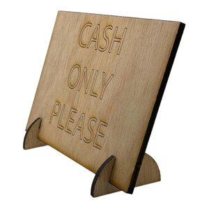 Może przedstawiać: Drewniany znak z podstawką, na kt&oacute;rym widnieje napis "CASH ONLY PLEASE" białymi literami.