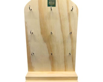 May include: A wooden display stand with a light-colored finish. It features a curved top and a small shelf at the base. Nine silver hooks are evenly spaced across the front. A small green and white label is at the top.