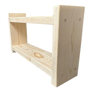 May include: A two-tiered, unfinished wooden shelf. The shelf is constructed from light-colored wood, with visible grain patterns. The design features two horizontal shelves supported by vertical side pieces, creating an open storage space. The shelf is ideal for displaying items.