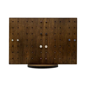May include: A wooden earring display stand with a circular base. The stand has multiple holes for displaying earrings. There are several pairs of earrings displayed on the stand, including blue, white, and pink earrings.