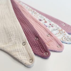 Pode incluir: Uma coleção de cinco babadores para bebês em vários tons de rosa e creme. Os babadores são feitos de tecido macio e texturizado e apresentam fechos de pressão. Um babador tem um padrão floral.