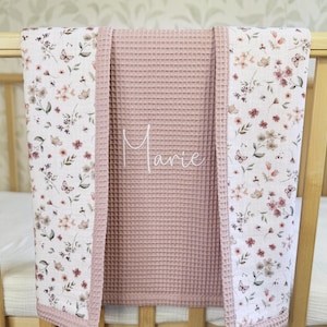 May include: A dusty rose waffle-knit blanket featuring a central panel with the name Marie embroidered in white script. The blanket is bordered by two side panels displaying a delicate floral and butterfly pattern in shades of pink and green.
