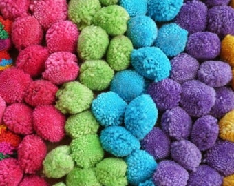 Può includere: Primo piano di una vibrante serie di pompon colorati. I pompon sono disposti in un gradiente di colori, tra cui sfumature di rosa, verde, blu, viola e giallo. La consistenza dei pompon è morbida e soffice, creando un display visivamente accattivante.