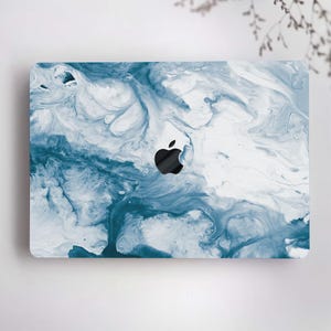 May include: A laptop case featuring a blue and white abstract marble design. The case has a glossy finish and a black Apple logo in the center. The design resembles flowing paint or water, creating a unique and artistic look.