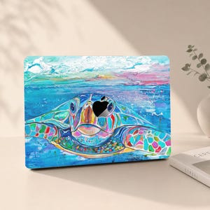 May include: A laptop skin featuring a vibrant, multi-coloured artistic illustration of a sea turtle swimming in blue water. The design incorporates shades of turquoise, pink, and yellow, with a central cutout revealing the Apple logo on the laptop.