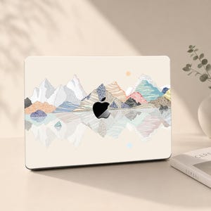 May include: A laptop skin featuring a cream-colored background with a stylized mountain range illustration. The mountains are rendered in various textures and pastel colors, including blue, orange, and white, with a reflection effect below.