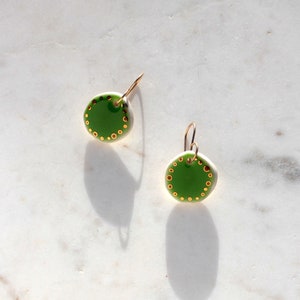 May include: A pair of green ceramic earrings with gold accents. The earrings are round and have a gold circle around the edge.