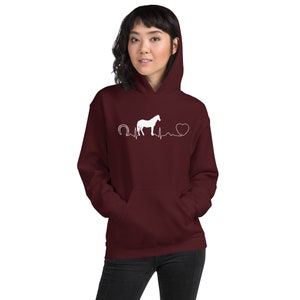 May include: A maroon hoodie with a white silhouette of a horse, a horseshoe, a heart, and a heartbeat line graphic. The text "Horseshoe Heartbeat" is printed on the hoodie.