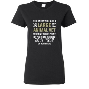 May include: Black t-shirt with a white and gold design that says "You know you are a large animal vet when at some point of your day you had cow poop on your head."