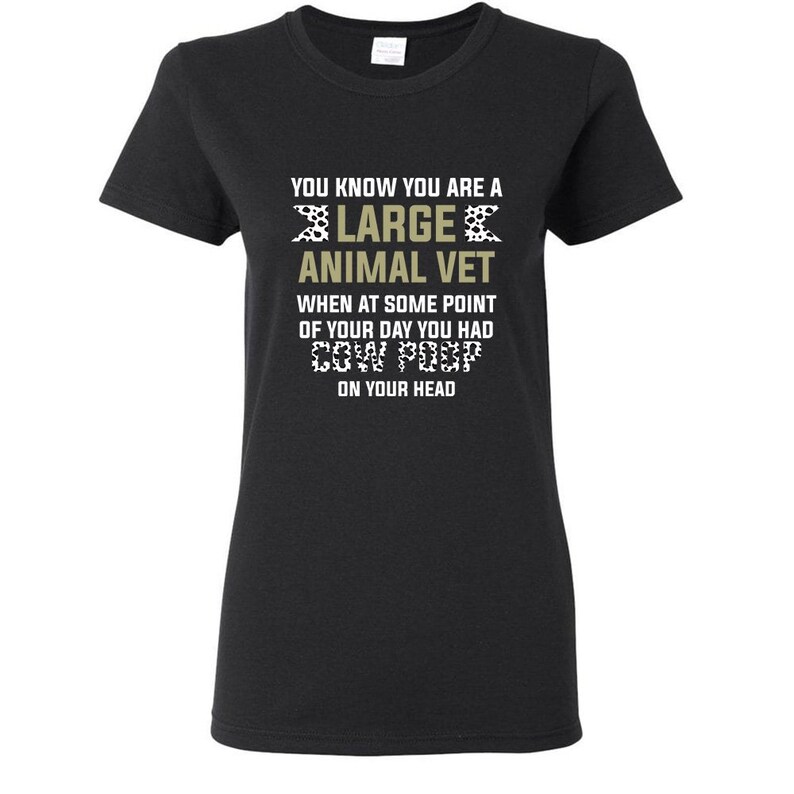 May include: Black t-shirt with a white and gold design that says "You know you are a large animal vet when at some point of your day you had cow poop on your head."