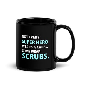 Puede incluir: Taza de café negra con texto blanco que dice "Not every super hero wears a cape... some wear scrubs."