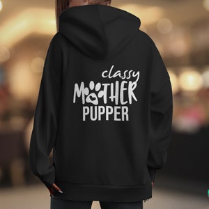 Może przedstawiać: Czarna bluza z kapturem z białym napisem "classy MOTHER PUPPER" i wzorem łapy. Bluza ma kaptur i długie rękawy. Zdjęcie zrobione jest od tyłu.