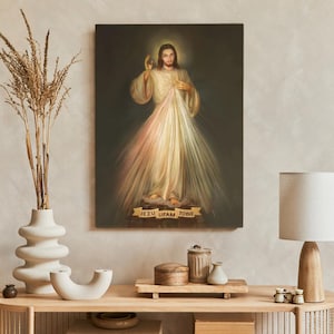 Puede incluir: Una pintura de Jesucristo con un halo dorado y rayos de luz que emanan de su cuerpo. La pintura está sobre un lienzo y tiene un marco de madera. El texto "Jezu Ufam Tobie" está escrito en una pancarta debajo de la pintura.