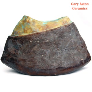 May include: A brown ceramic bowl with a textured surface and a turquoise glaze. The bowl is shaped like a mountain and has a wide opening.