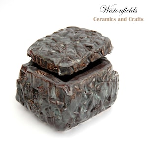 May include: A dark brown ceramic box with a textured surface and a lid that is slightly ajar. The box is made by Westonfields Ceramics and Crafts.