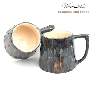 May include: Two ceramic mugs with a dark blue glaze and white speckles. One mug has a textured exterior and the other has a smooth exterior. The mugs are made by Westonfields Ceramics and Crafts.